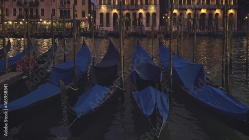 Gondolas floating on waters of Grand canal in Venice, Italy, at night. Frontal shot of parked boats with blue covers, medieval buildings in background