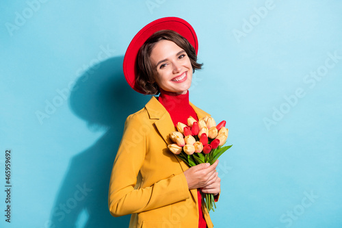 Photo of sweet charming young woman dressed red headwear holding bouquet smiling isolated blue color background