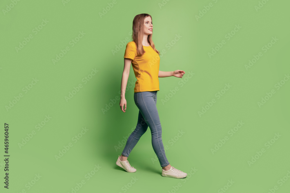 Profile portrait of nice positive lovely lady empty space walk wear yellow t-shirt jeans sneakers on green background Profile portrait of nice positive lovely lady empty space walk wear yellow t-shirt jeans sneakers on green background