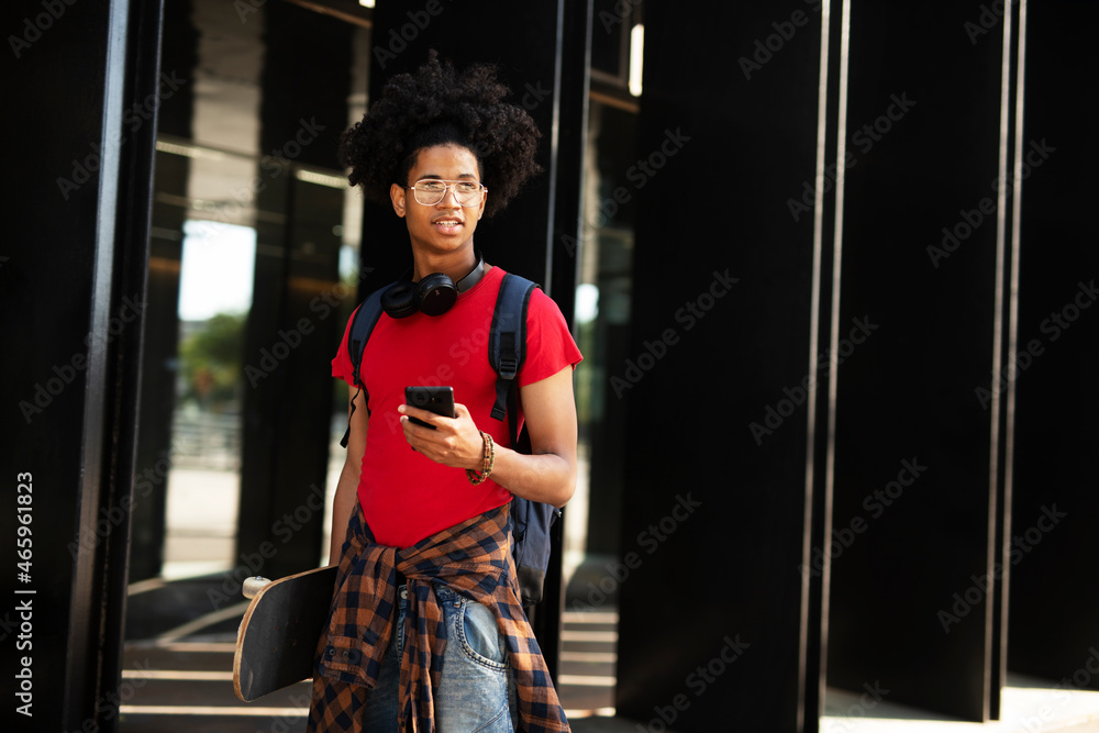 Happy african-american man with skateboard. Young fashion man using the phone while walking through the city. Happy african-american man with skateboard. Young fashion man using the phone while walking through the city.