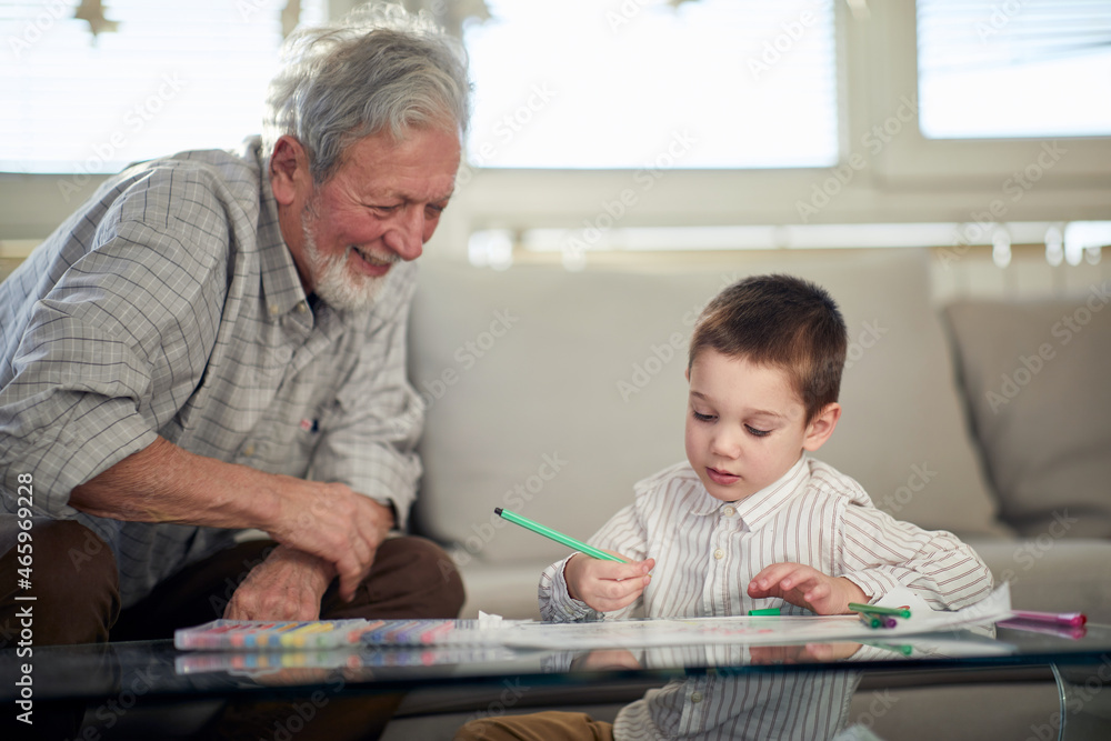A little grandson enjoys drawing while spending a quality time with his grandpa at home. Family, home, playtime A little grandson enjoys drawing while spending a quality time with his grandpa at home. Family, home, playtime