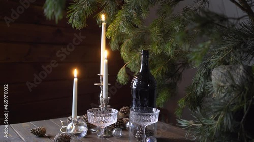 Vintage wooden table in Scandinavian style served vine bottle and glasses before celebrating Christmas holiday. Decorated fir twig, advent transparent baubles and burning candles , lateral motion shot photo