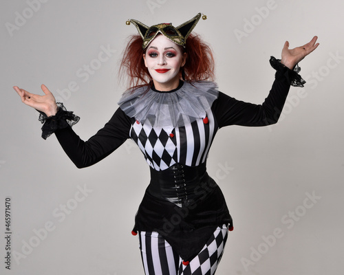 close up portrait of red haired girl wearing a black and white clown jester costume, theatrical circus character. Standing pose isolated on studio background.
