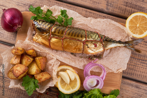 Composition smoked mackerel fish with garnish potatoes lemon greens onions served on wooden board plate top view