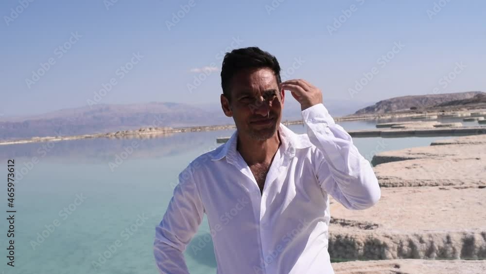 Man in white shirt stay on background original, stone, salt islands in sea. Person smoothes hair. Summer, vacation, travel. Interesting seascape. Outdoors. Man in white shirt stay on background original, stone, salt islands in sea. Person smoothes hair. Summer, vacation, travel. Interesting seascape. Outdoors.