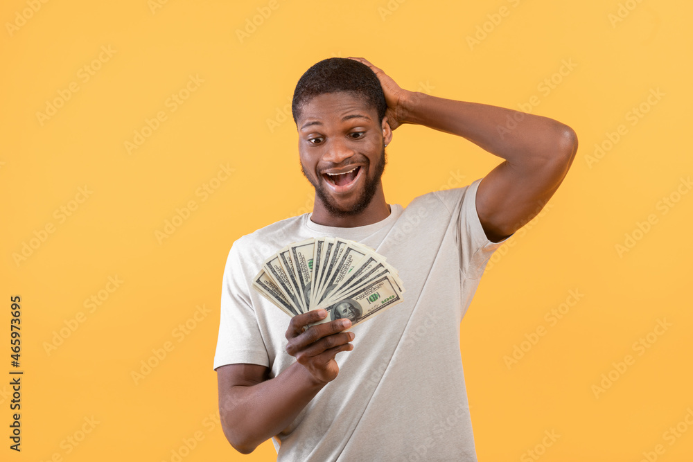 Big luck concept. Overjoyed african american man holding money, shouting and touching head, yellow background Big luck concept. Overjoyed african american man holding money, shouting and touching head, yellow background