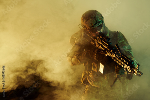 Portrait of airsoft player in professional equipment with machine gun in abandoned ruined building. Soldier with weapons at war in smoke and fog photo