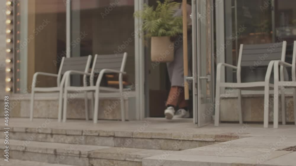 Locked-down low angle of restaurant workers taking flower pots and arranging them outdoors in morning before opening Locked-down low angle of restaurant workers taking flower pots and arranging them outdoors in morning before opening