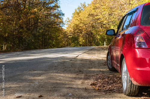 Red car standing on the side of a country road against the background of an autumn forest. Travel concept.