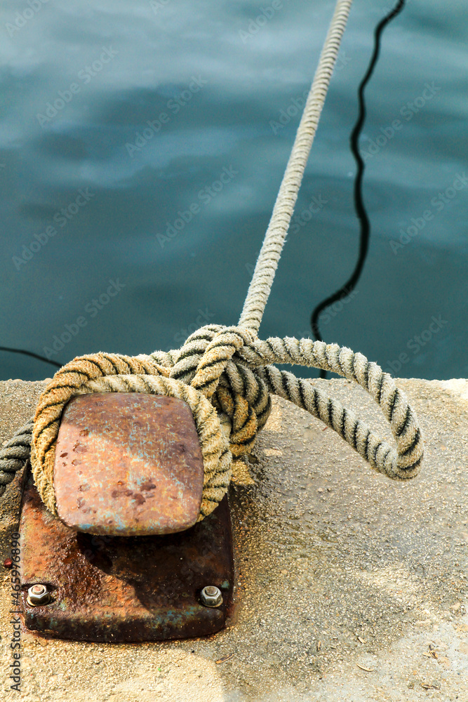 Fototapeta premium Rusty mooring bollard with tied rope in the port
