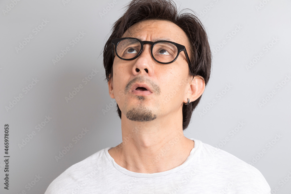 Asian man wearing eyeglasses with surprise and wonder expression on grey background. Asian man wearing eyeglasses with surprise and wonder expression on grey background.