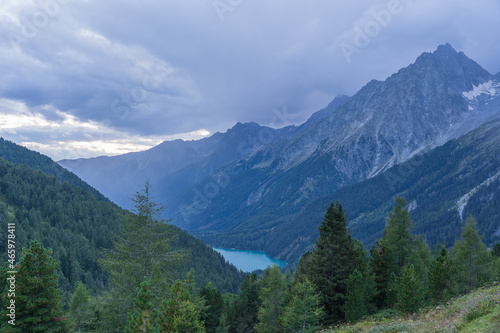 Landscape of Hochgall mountain peaks covered by clouds, valley and Antholzer See lake in Dolomites, Italy
