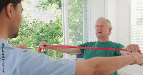 Caucasian senior man holding resistance band exercising with male physiotherapist at nursing home photo