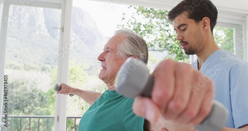 Male physiotherapist looking at senior man exercising with dumbbells in retirement home photo