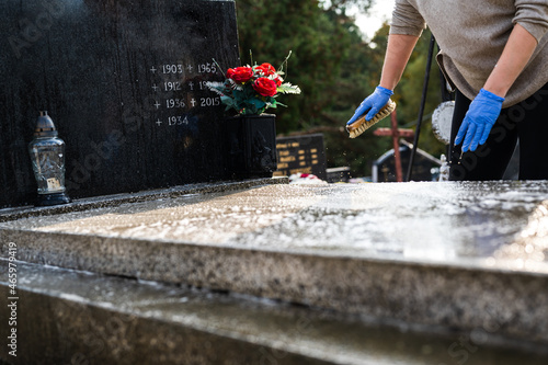 Unrecognizable woman washing the tombstone with a brush. Graveyard preparation for All Saints Day.