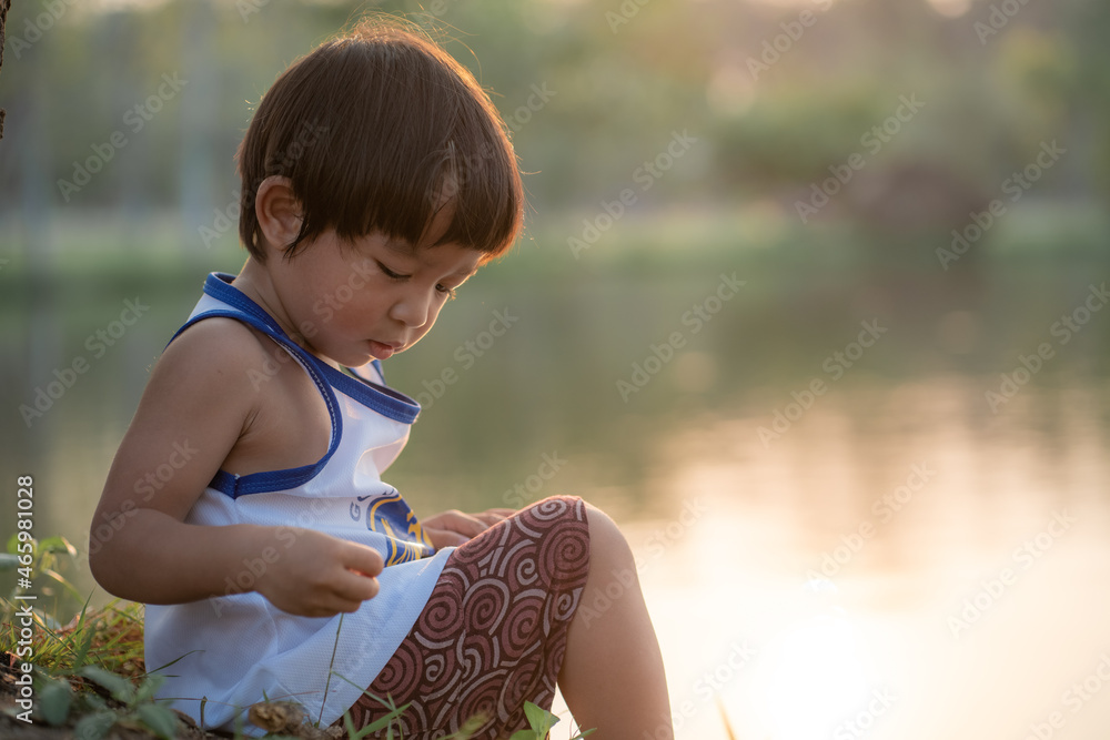 Asian boy sitting under tree sunset time lookimg to the river summer recreation