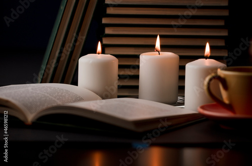 study table with candles with flame and reading book and partial view of cup, (focus on candle).