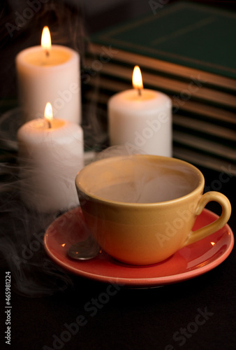 cup of coffee with smoke and candles alfon with books (focus on cup).