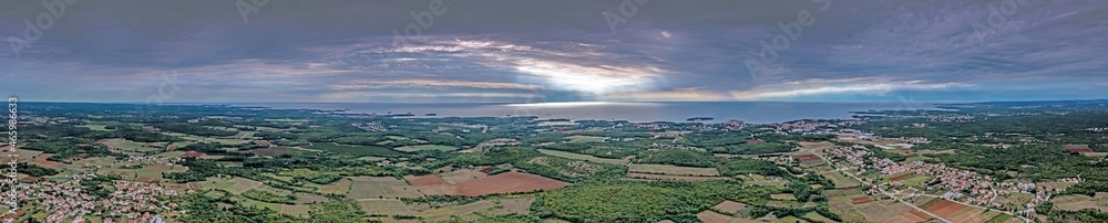 Drone panorama over Istrian Adriatic coast near Porec taken from high altitude during daytime with cloudy sky and impressive sun rays