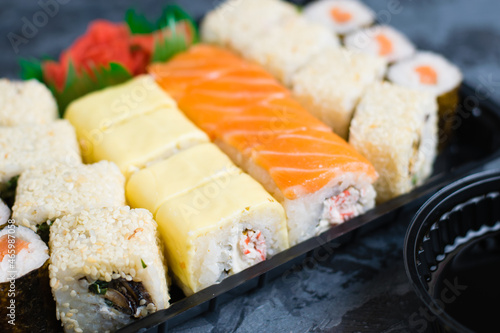 Sushi set, maki with red fish, rice and nori, rolls with mussels, sesame cheese and crab stick, Philadelphia roll with salmon. Sushi sticks, soy sauce and wasabi in plastic wrap.