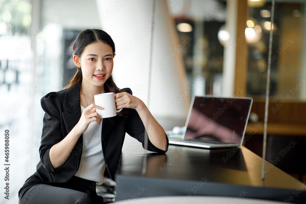 Young smiling Asian businesswoman staying with disposal cup of coffee Young smiling Asian businesswoman staying with disposal cup of coffee