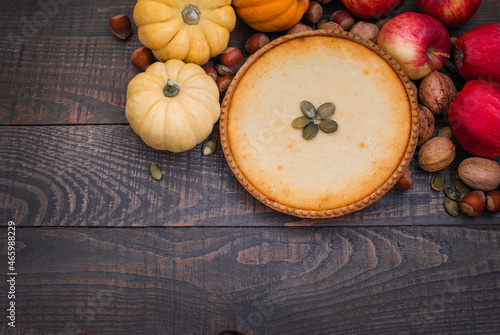 Pumpkin pie surrounded by pumpkins, walnuts and apples on a dark wooden background.