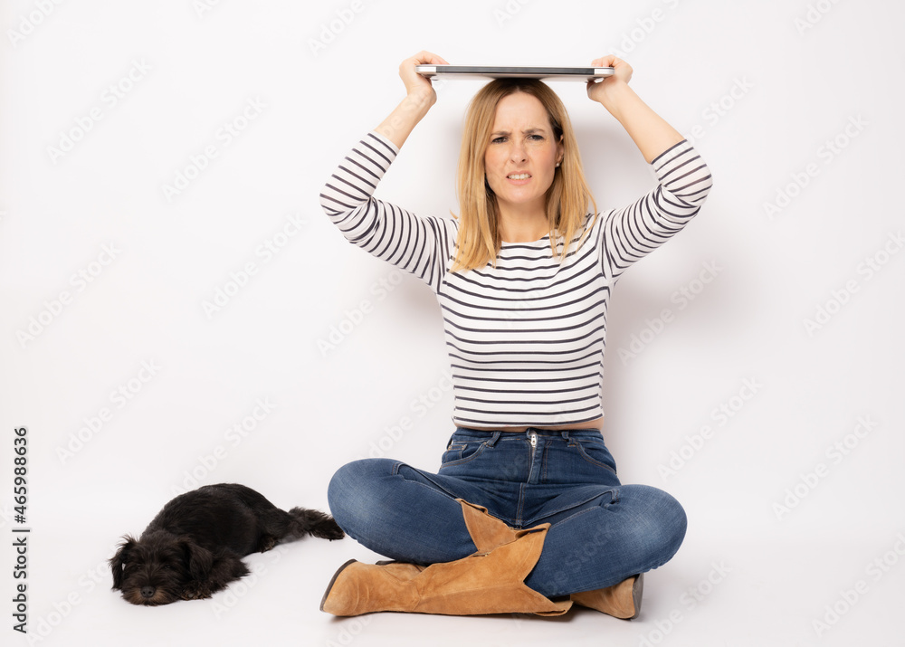 Photo of young angry woman sitting on floor with laptop on head and little dog companion isolated white background Photo of young angry woman sitting on floor with laptop on head and little dog companion isolated white background