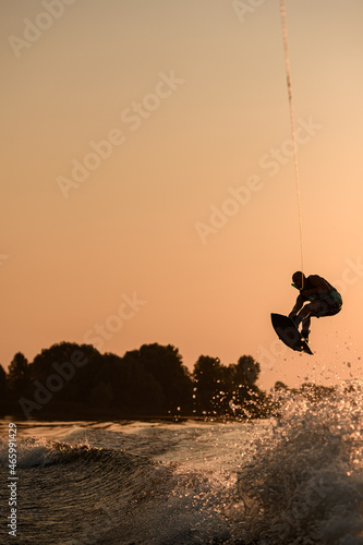 great view of active male rider holds rope and making jump on wakeboard at evening sky on background.