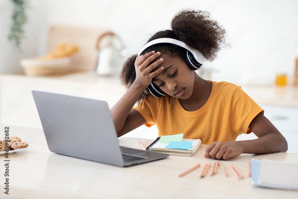 Upset black school girl doing homework, kitchen interior