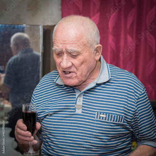 Elderly man with a glass of red wine in a striped polo