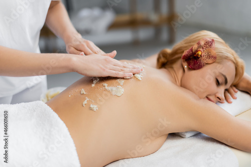 masseur applying body scrub on back of client on massage table