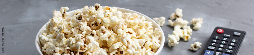 banner of A white bowl of popcorn and TV remote on a grey background. The concept of watching TV, film banner of A white bowl of popcorn and TV remote on a grey background. The concept of watching TV, film