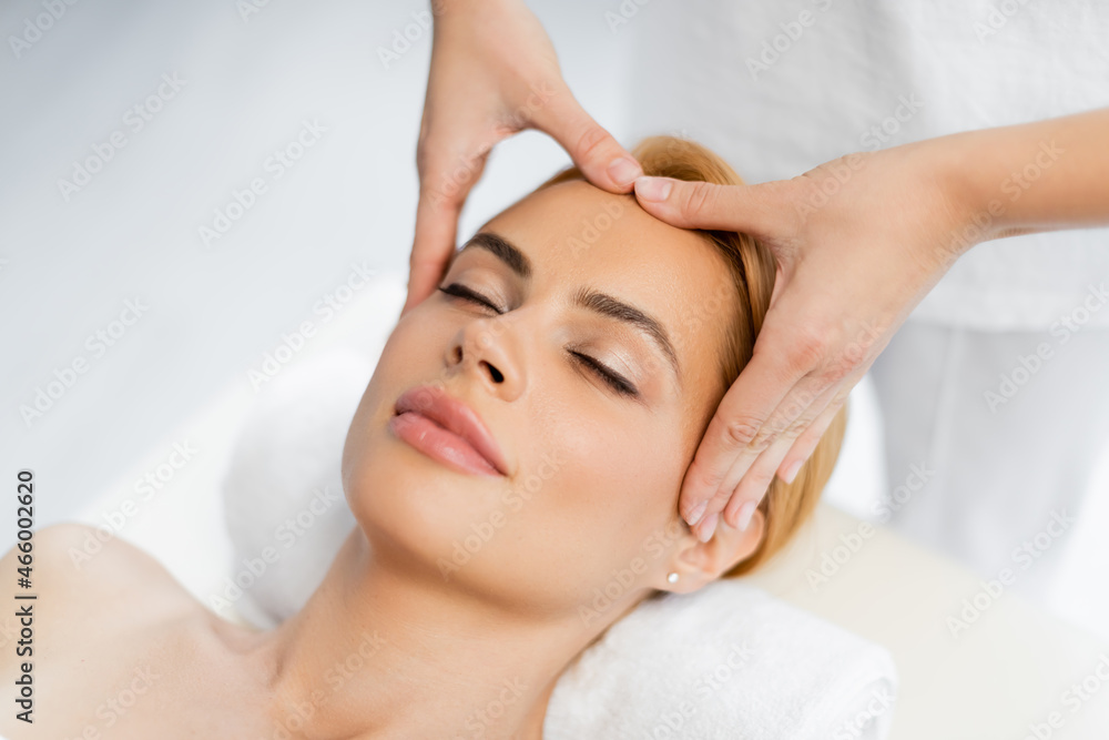 high angle view of masseur doing face massage of blonde client with closed eyes