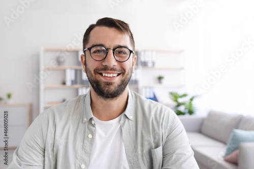 Headshot of cheerful mature european man with beard in glasses look at laptop webcam at minimalist living room