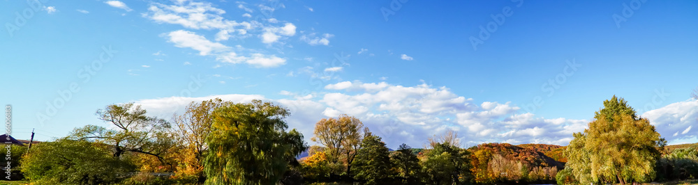 panorama of trees, white clouds over the mountains, early autumn, blue sky panorama of trees, white clouds over the mountains, early autumn, blue sky