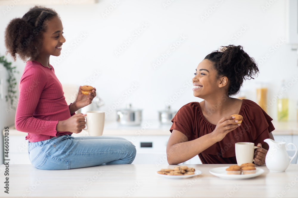 Cheerful african american mom and daughter drinking tea with cupcakes Cheerful african american mom and daughter drinking tea with cupcakes