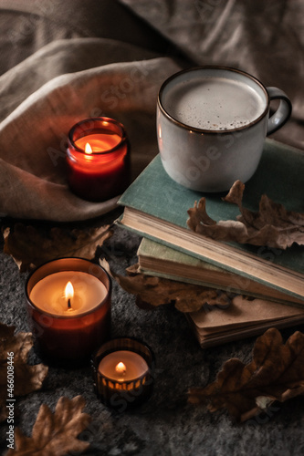 old books, coffee cup and burning candles with dry oak leaves on a stone background