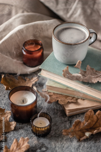 old books, coffee cup and candles with dry oak leaves on a stone background