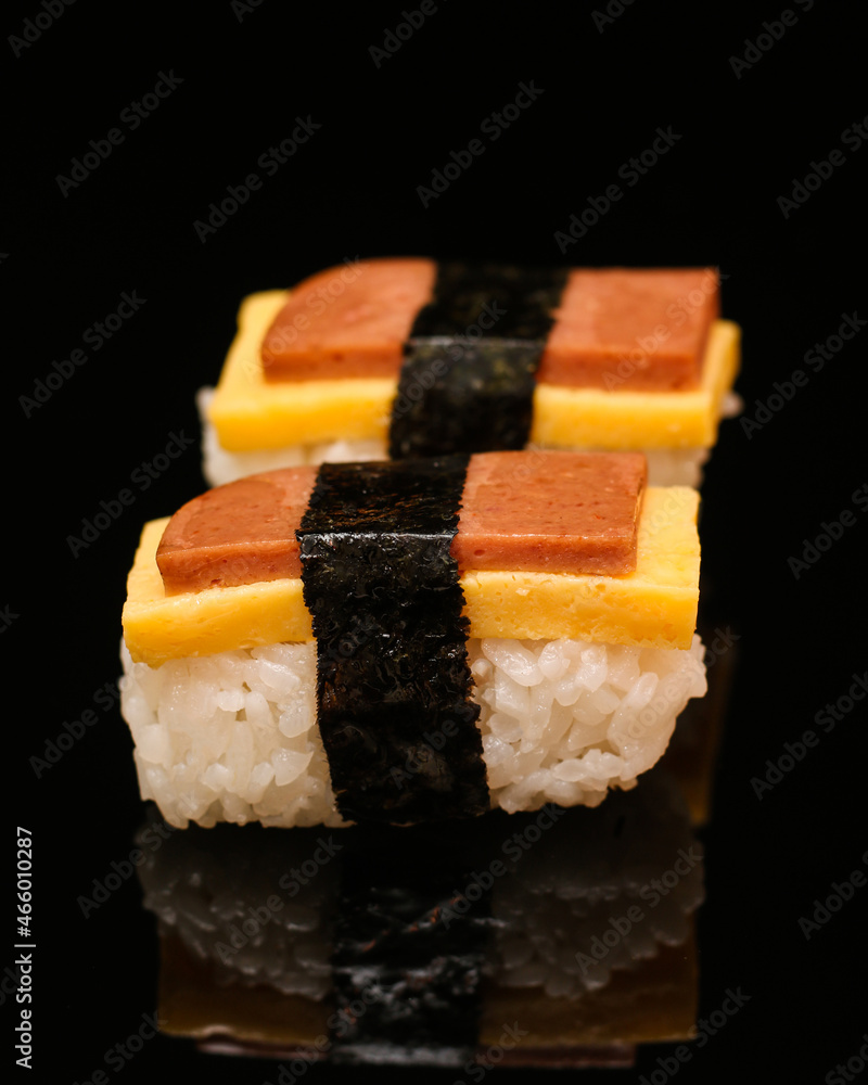 Egg sushi with a slice of ham on a black reflective background Egg sushi with a slice of ham on a black reflective background