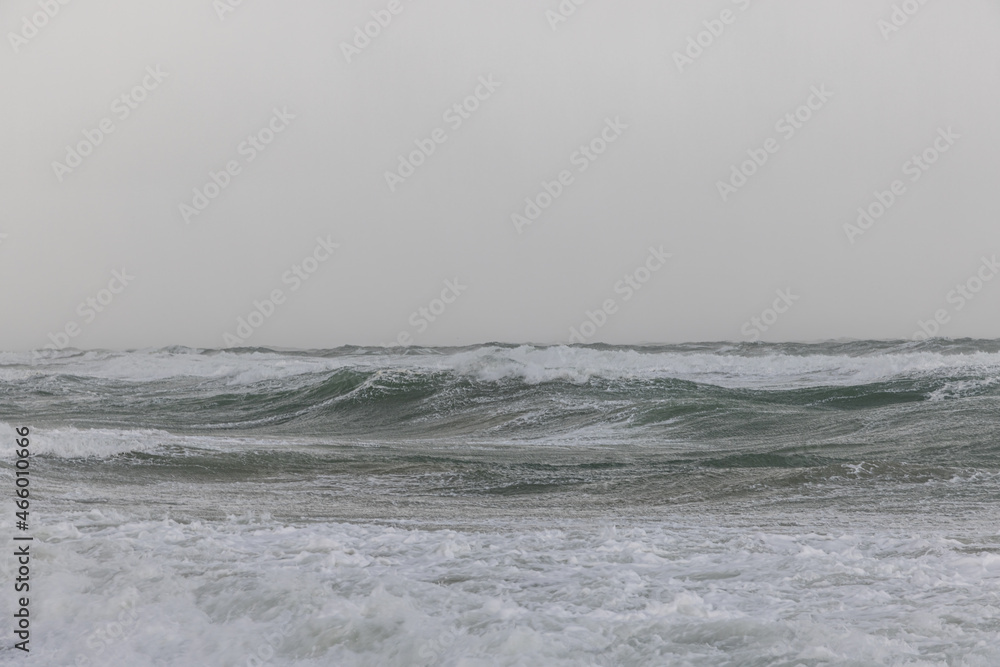 A dramatic view of a very choppy sea with huge crashing waves during a major storm under a grey sky A dramatic view of a very choppy sea with huge crashing waves during a major storm under a grey sky