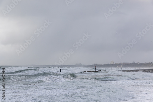A dramatic view of a very choppy sea with huge crashing waves on groynes (breakwater) during a major storm under a grey sky