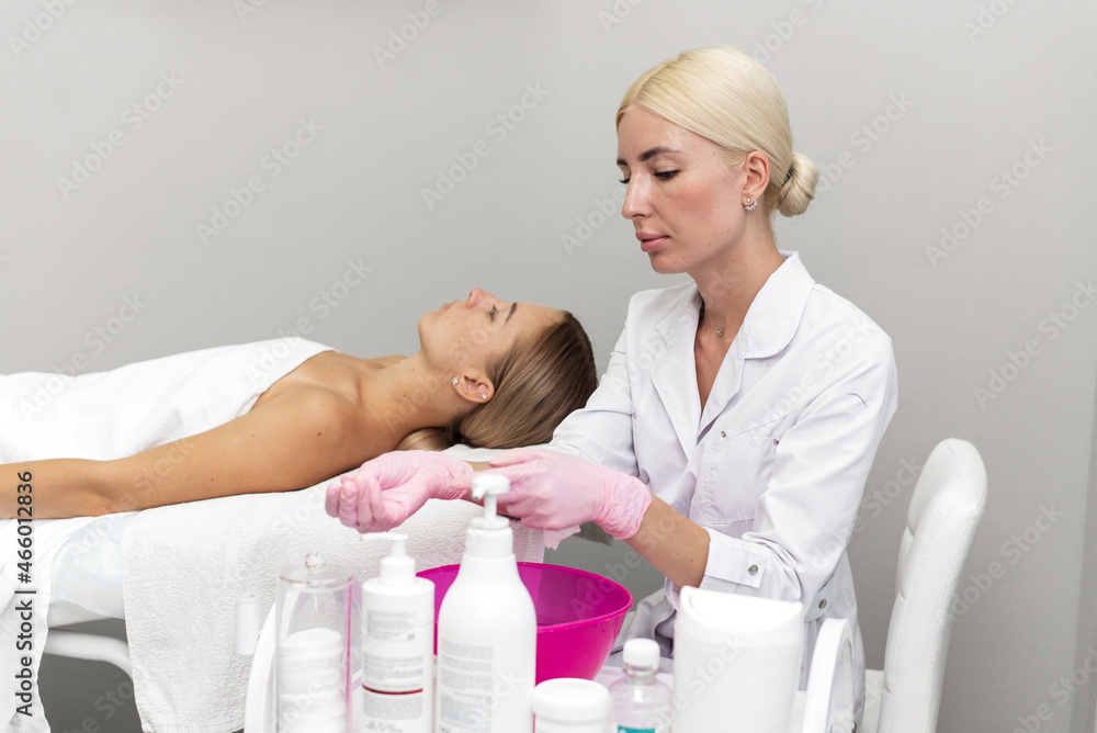 A beautiful woman beautician puts on gloves on her hands while the client lies on the couch and waits for the procedure A beautiful woman beautician puts on gloves on her hands while the client lies on the couch and waits for the procedure