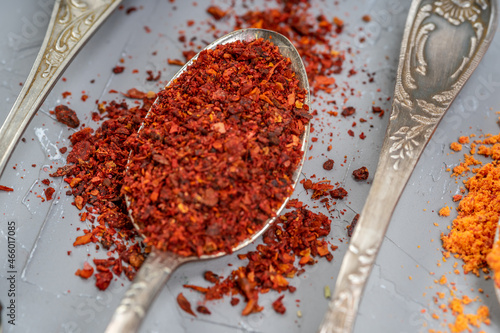 Red chili powder or paprika in a spoon on a gray background, close-up. Cooking ingredients, flavor.