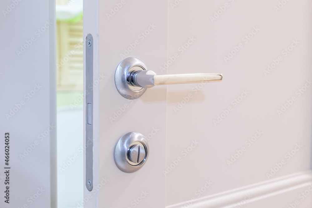Slightly open white door to the bathroom with a metal magnetic lock. Chrome-plated handle on the interior door. Silent magnetic lock on the interior door. Slightly open white door to the bathroom with a metal magnetic lock. Chrome-plated handle on the interior door. Silent magnetic lock on the interior door.