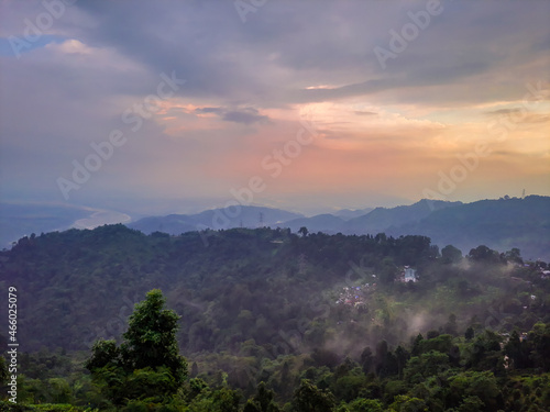 dramatic sunset orange sky over mountain range and green forest at evening from hill top