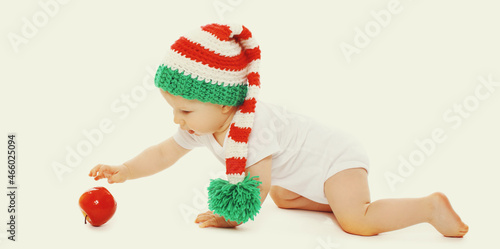 Baby crawling in knitted hat playing with red apple toy on white background