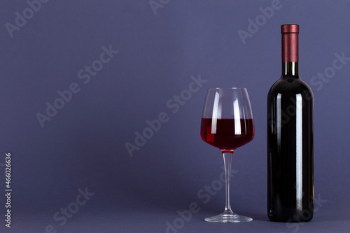 Closed bottle of red wine and a glass on a lilac background. With space for text.
