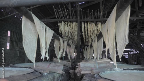 tthe boiling of soybean milk in copper pans over a mild fire in the workshop.  Sheets of yuba are hanging in two-fold over sticks several feet or more above the pans. photo