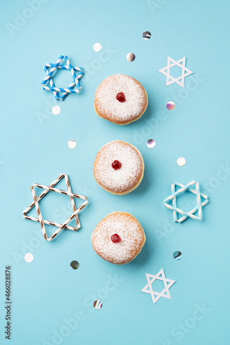 Jewish holiday Hanukkah concept - Hanukkah sweet doughnuts sufganiyot with powdered sugar and fruit jam, festive stars on blue paper background.