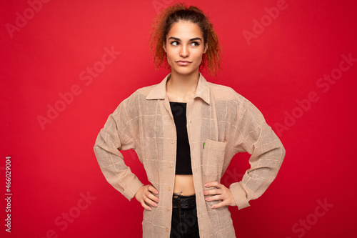 Shot of young beautiful thougtful curly woman poising isolated on background wall with copy space wearing casual beige shirt having doubts. Positive concept photo